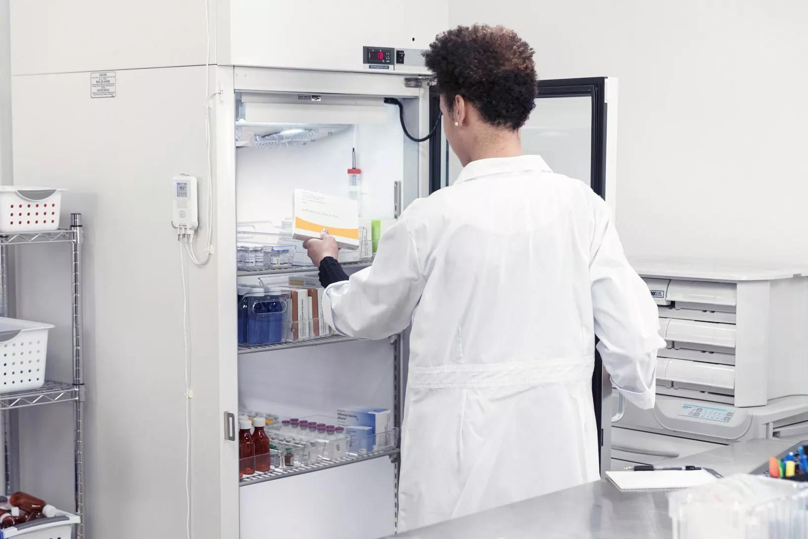 A pharmacist placing temperature-sensitive materials into a medication fridge while the T15e digital data logger monitors temperature.