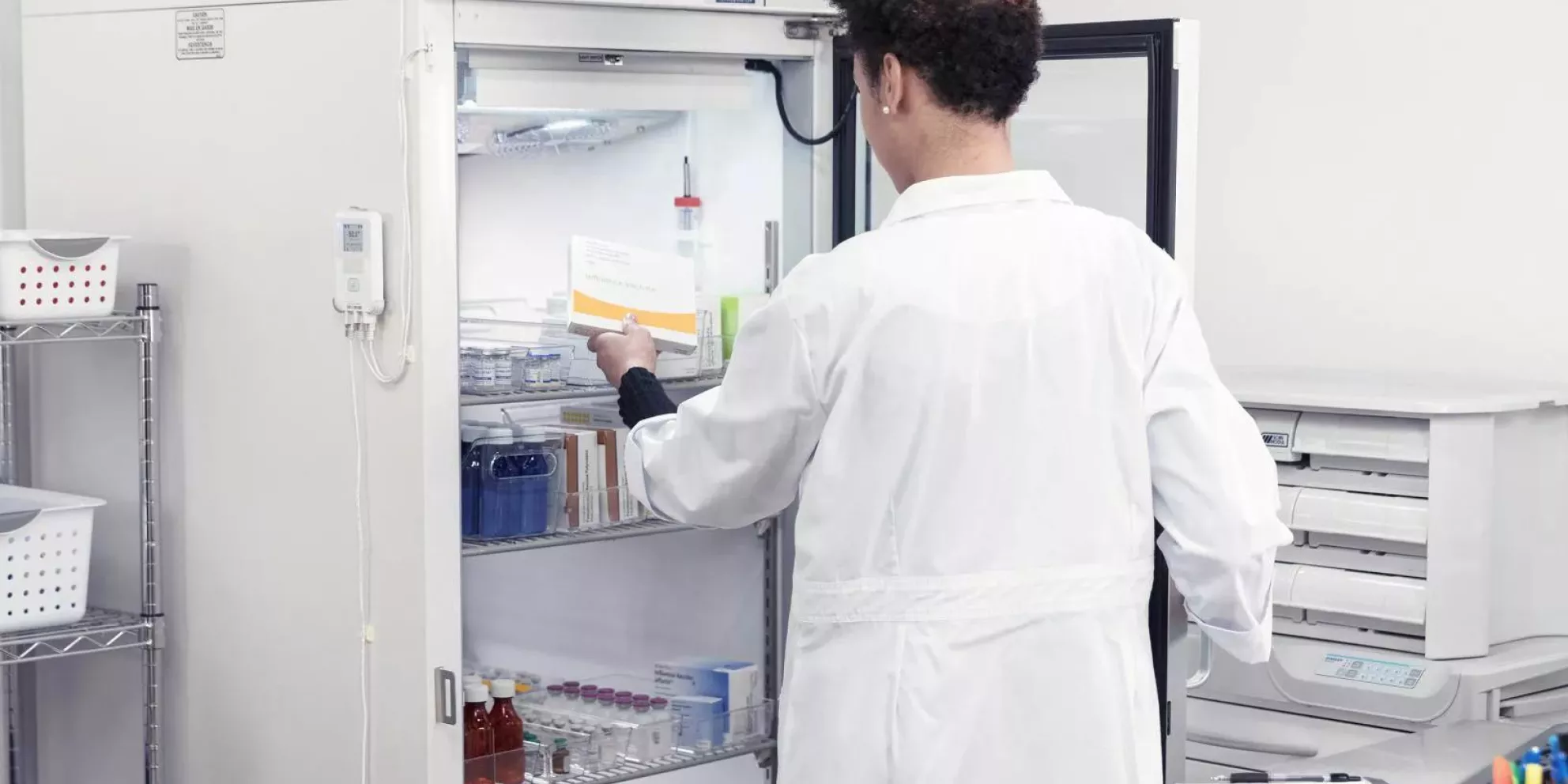 A pharmacist placing temperature-sensitive materials into a medication fridge while the T15e digital data logger monitors temperature.